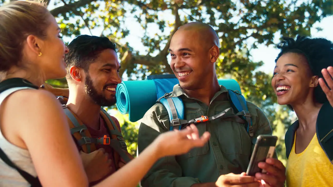 Group Of Lost Friends With Backpacks Using GPS On Mobile Phone On Vacation Hiking In Countryside