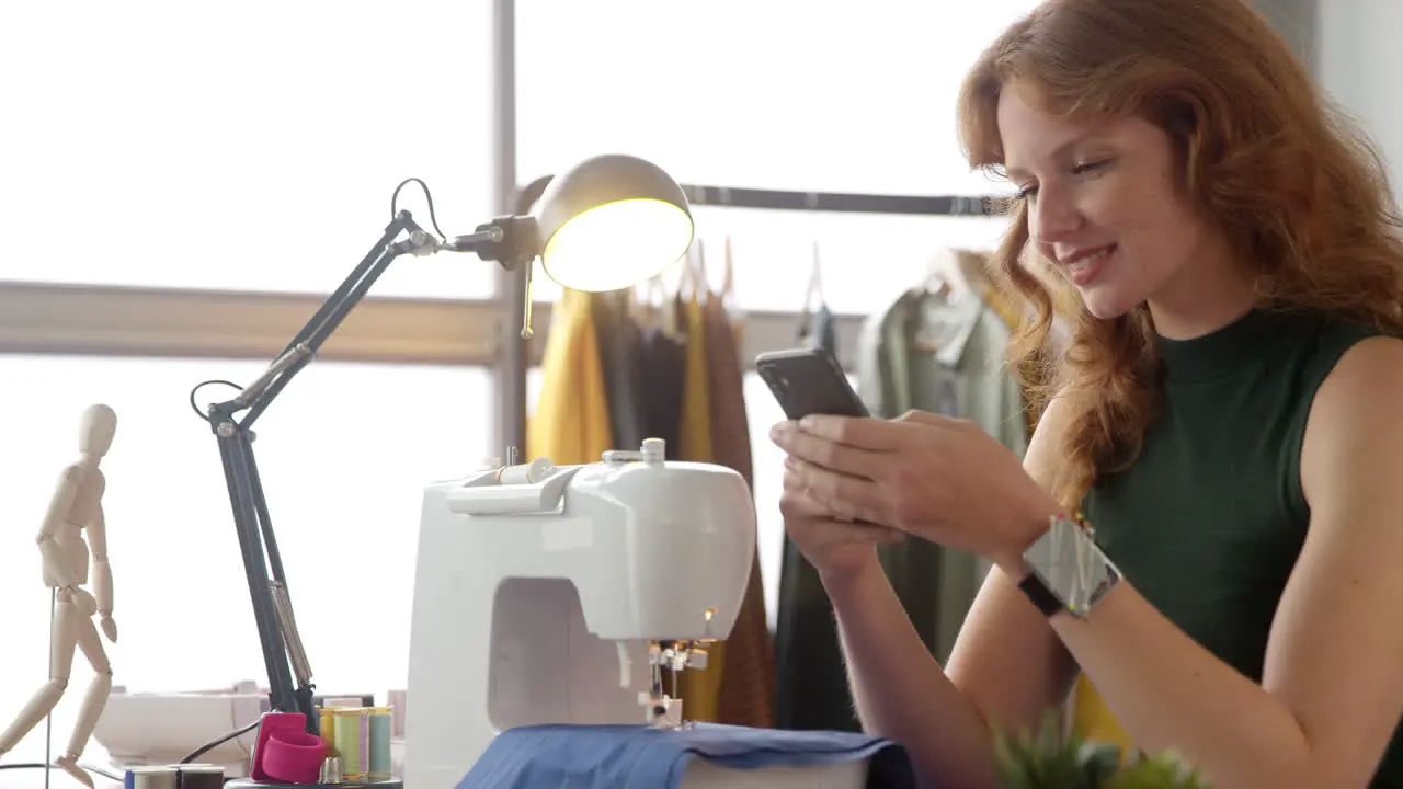 Female Owner Of Fashion Business Using Mobile Phone At Sewing Machine In Studio