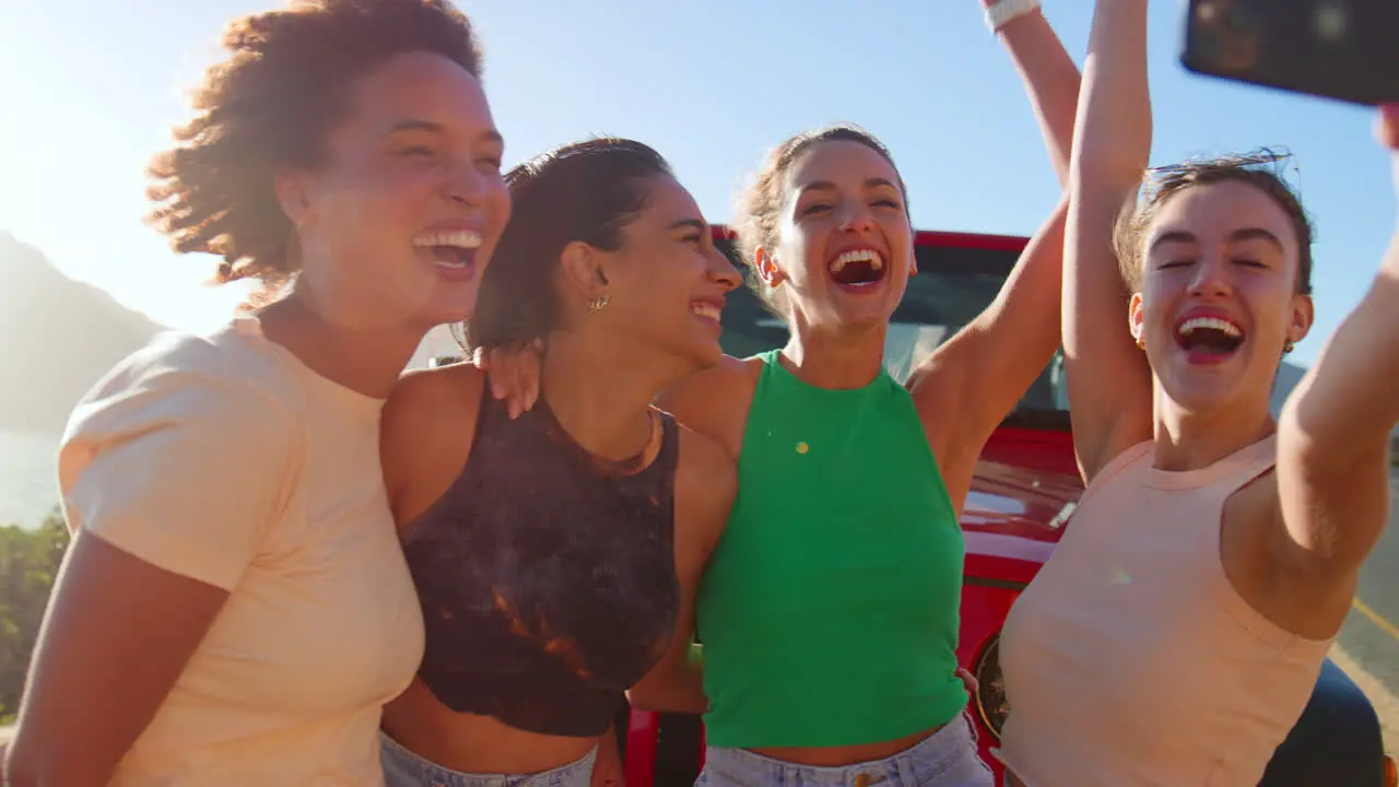 Portrait Of Laughing Female Friends Having Fun Posing For Selfie In Front Of Car On Road Trip