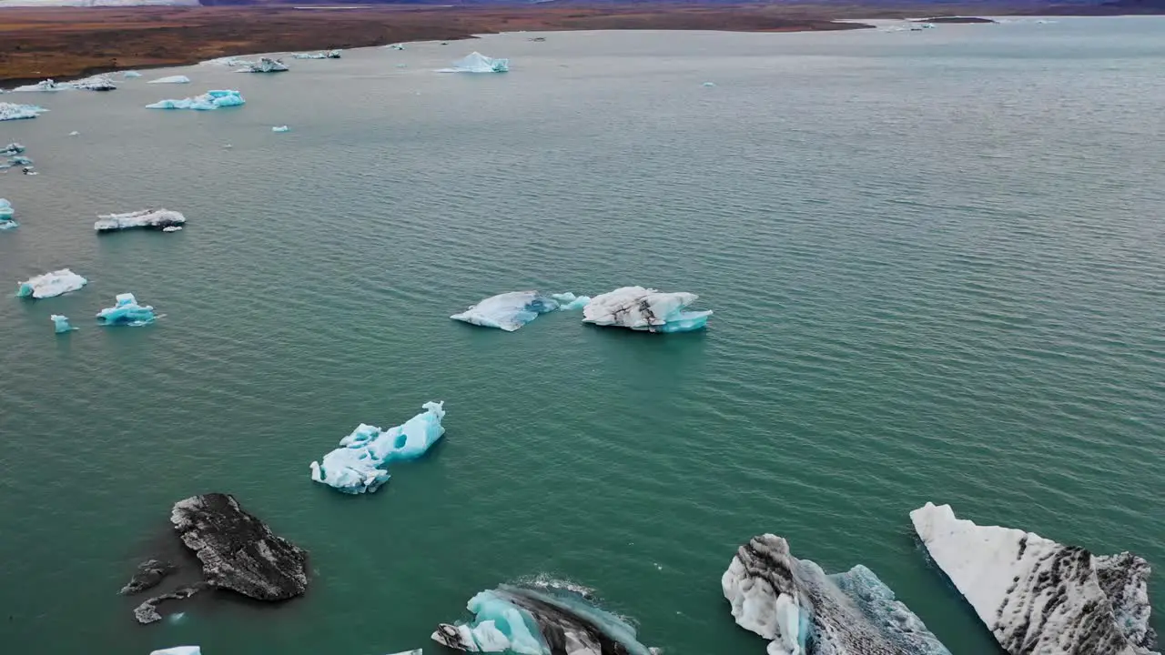 Flyover of icebergs in Jokulsarlon with horizontal flight and pan up to Vatnajokull icecap