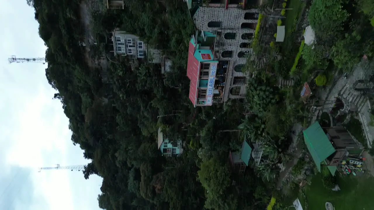 Drone portrait view in Guatemala flying in showing a hotel on a green hill and a blue lake surrounded by mountains on a cloudy day in Atitlan