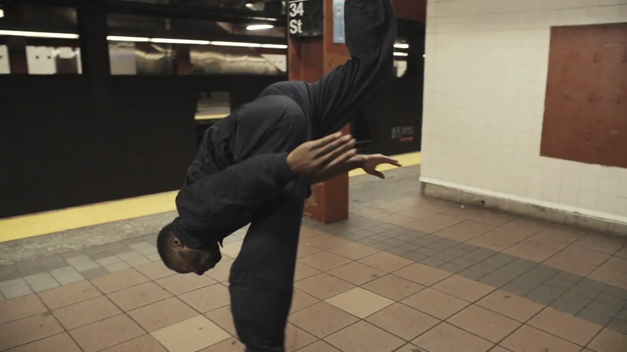 Janitor dancer flips on subway platform as steadicam wraps around as train pulls away