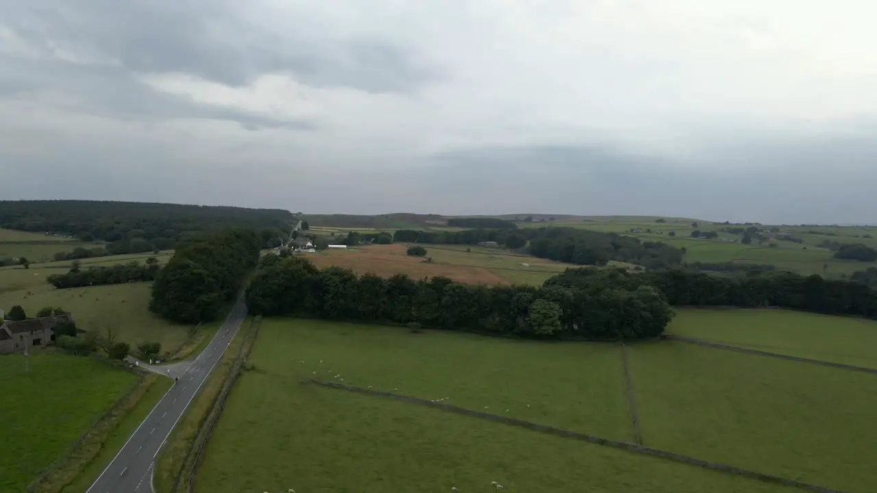 A 4K drone shot flying over Ringinlow road in the Peak District near Sheffield the sky is cloudy and green fields are on wither side of a long straight road