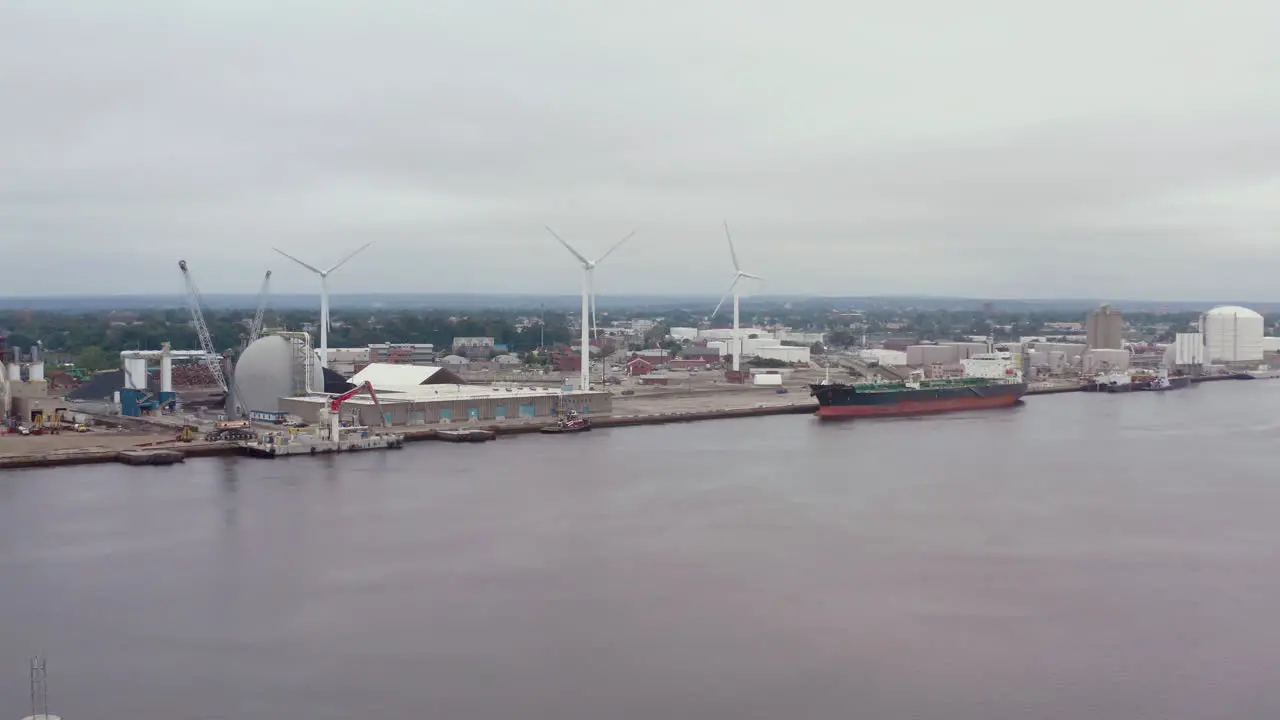 Cargo Ship Docked At The Port With Wind Turbines On A Cloudy Day