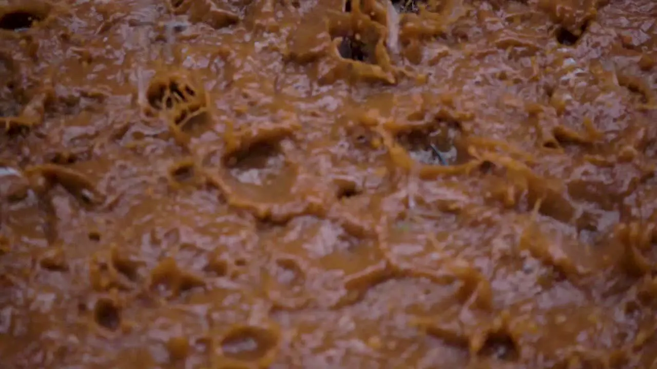 Close up slow motion shot of heavy rain falling into a muddy puddle and creating splashes