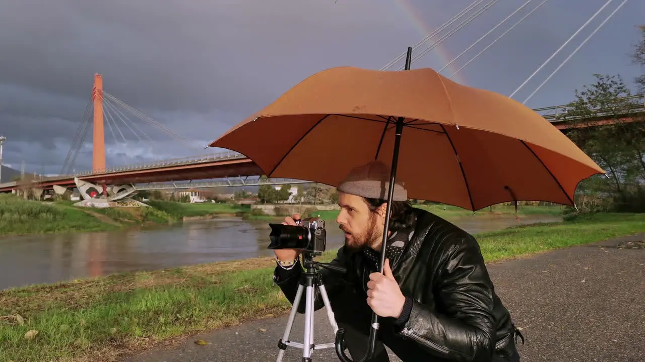 Caucasian photographer takes pictures under his umbrella during a rainy day while smiling