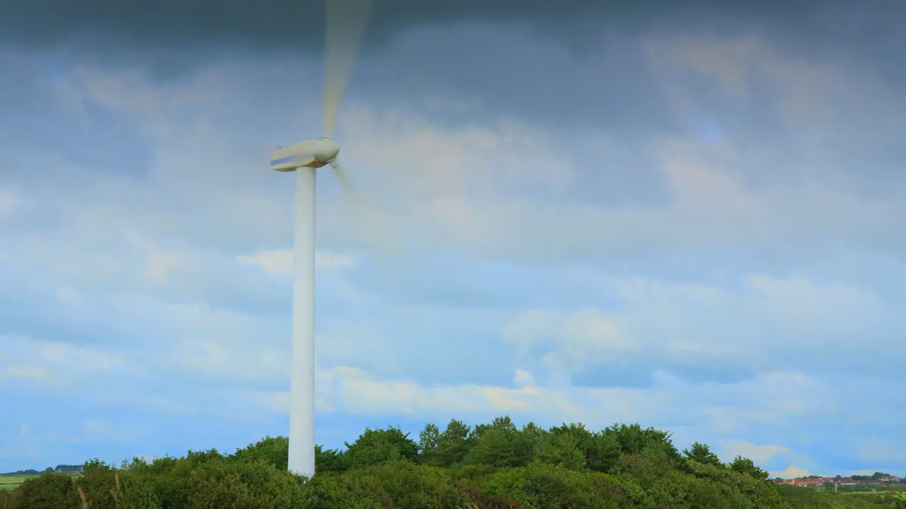 Windmill spinning and clouds racing by with cloud shadows on tree line