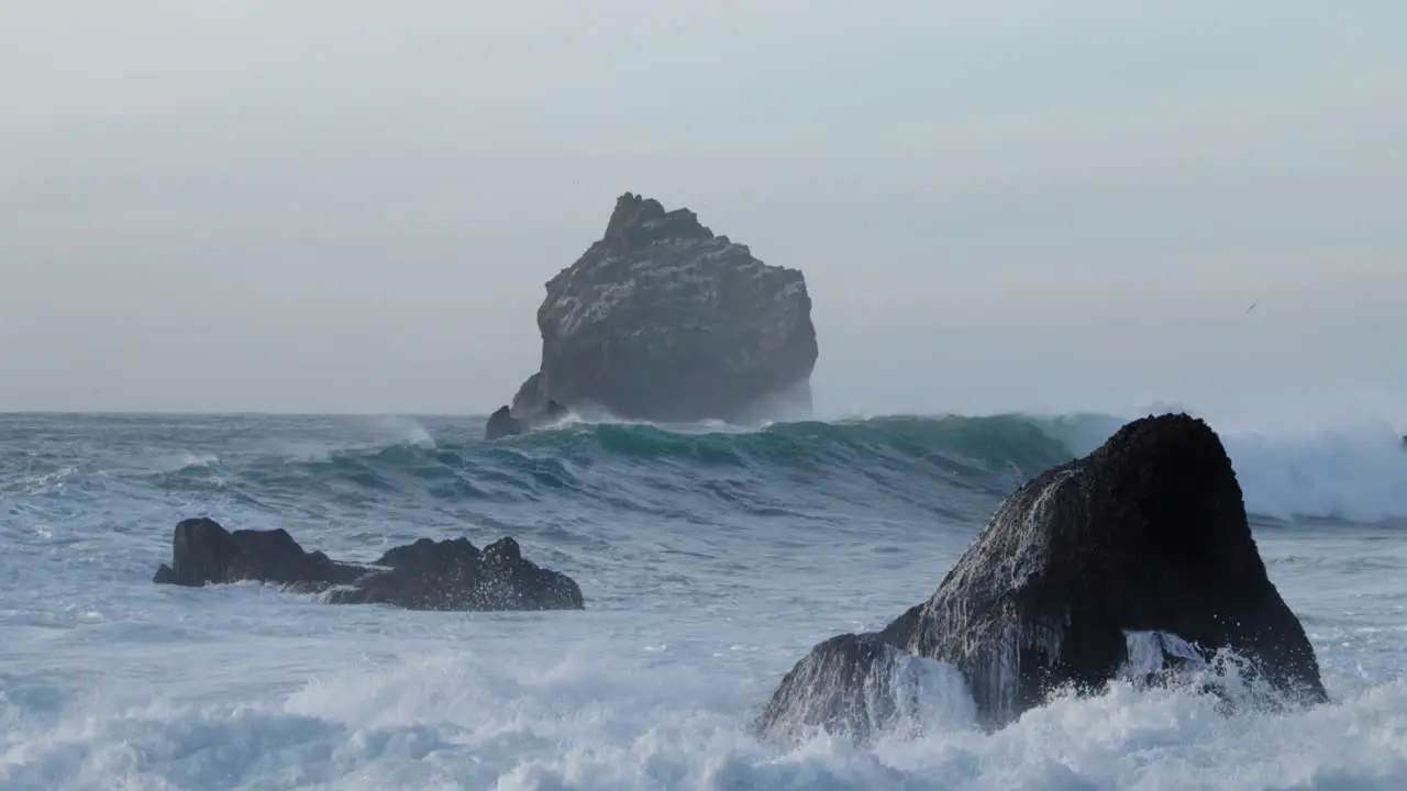 Rugged wild basalt rock formation with large waves breaking on shore mysterious scene