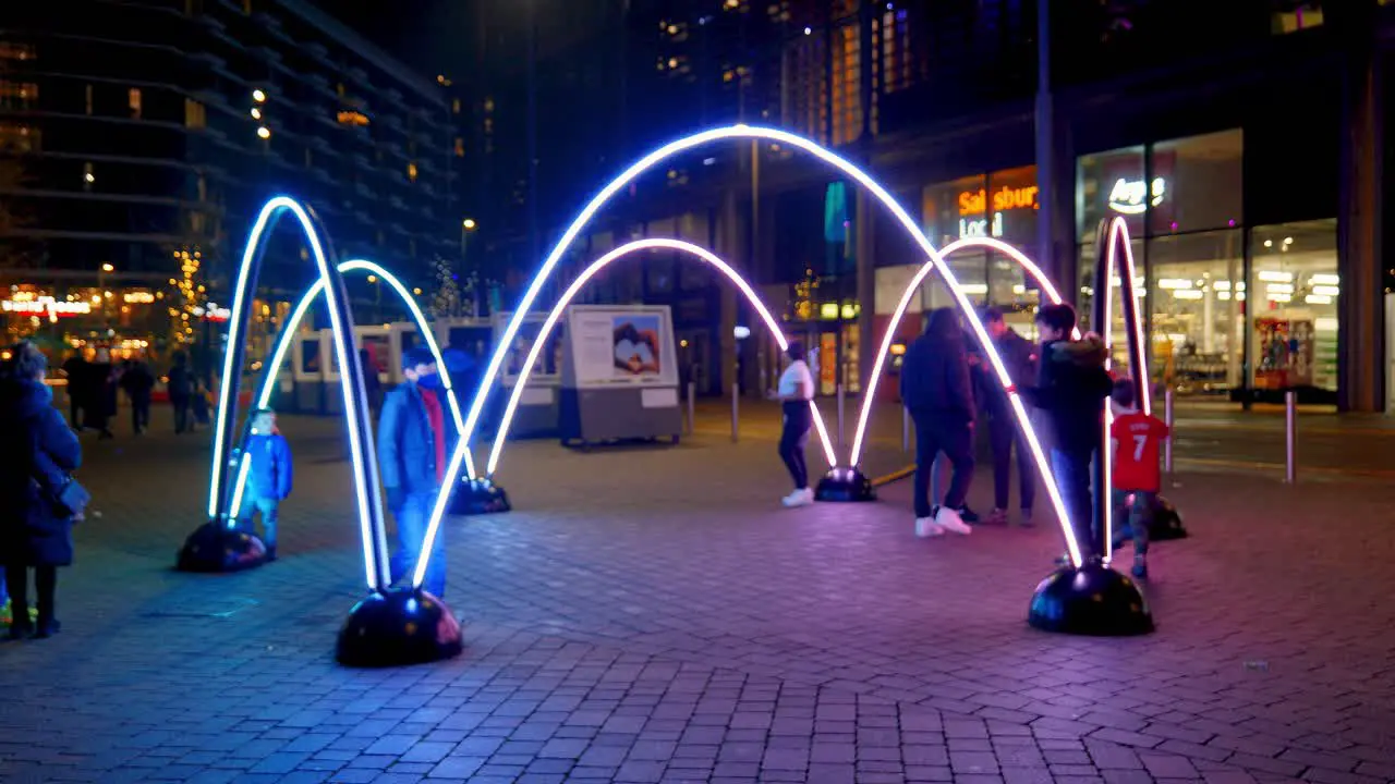 Visitors interacting with colourful Winterfest LED illuminated arches artwork installation at Wembley park at night