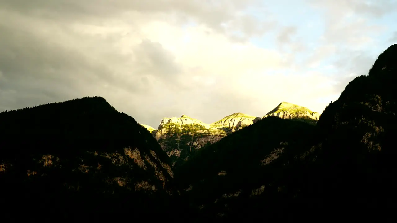 Dramatic clouds cross the sky as the sun sets beyond the rugged mountains