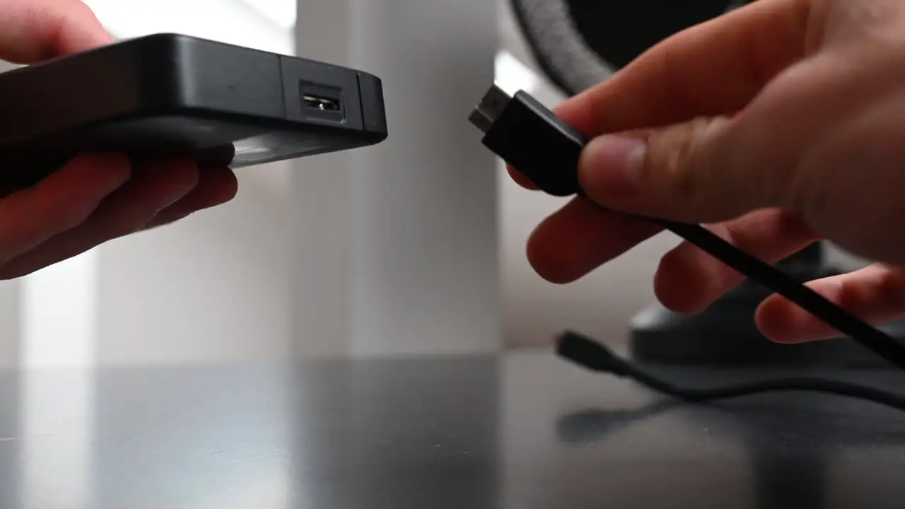 An electronice device user unplugs a black cable of an external hardrive and puts it on his desk