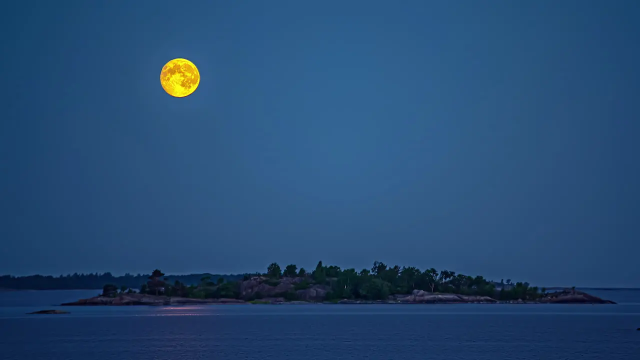 The full moon setting over a islet in a calm sea nighttime time lapse