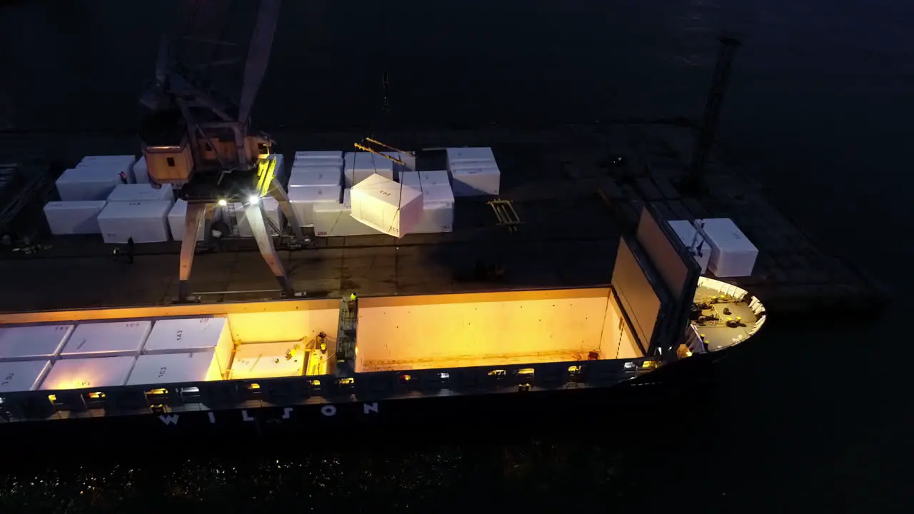 Crane loading the hull of a cargo ferry at nighttime aerial orbit