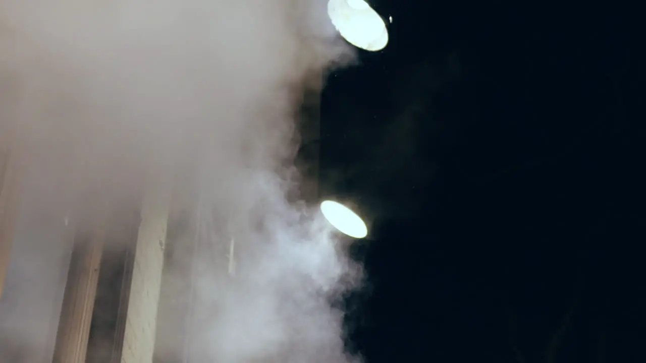 Steam rising in slow motion at night towards potlights