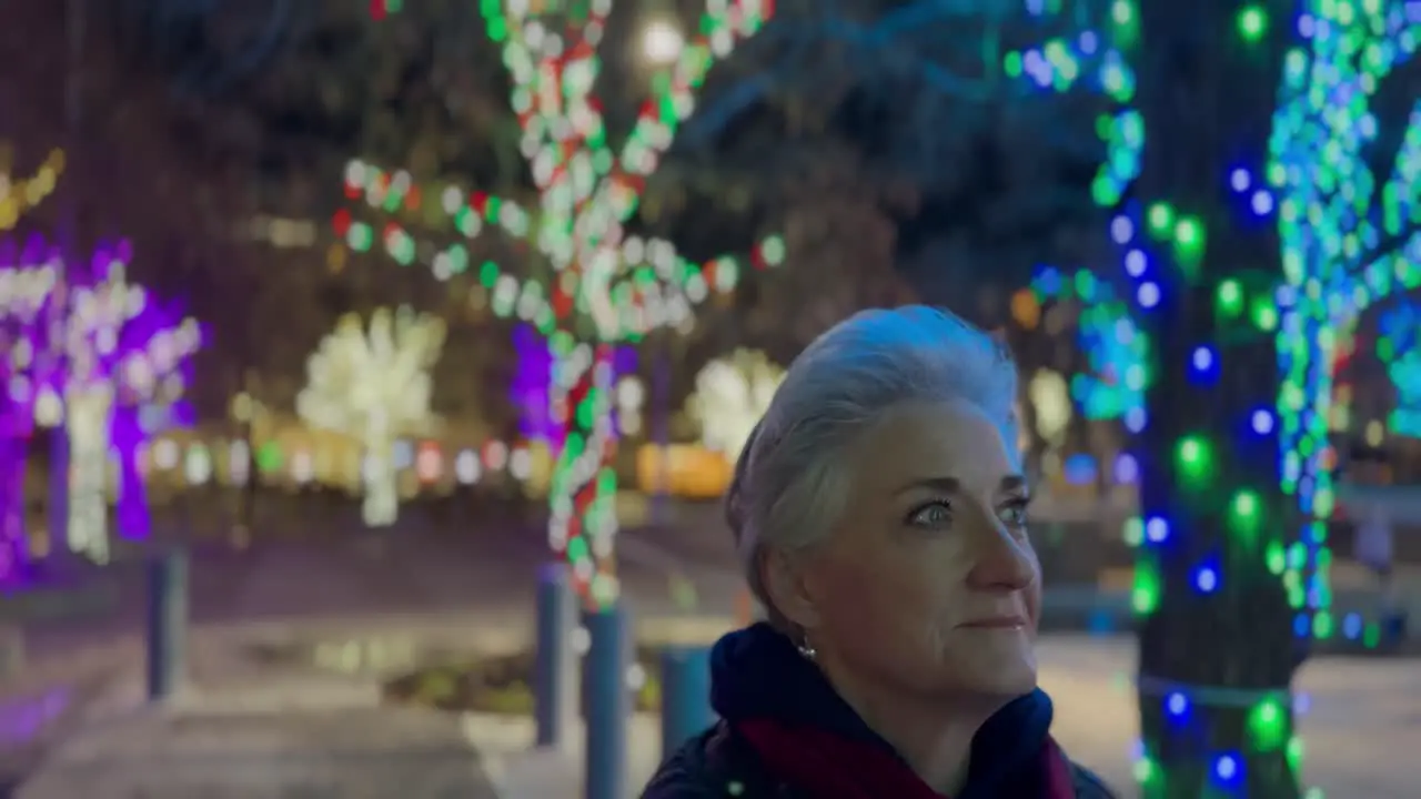 Senior woman walking at night in a city decorated with glowing Christmas lights