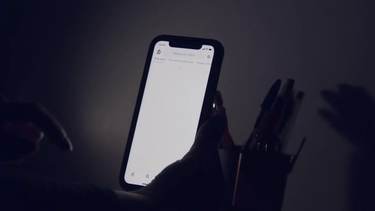 The glowing screen of a smartphone as a woman's hand opens the scrols her Twitter feed