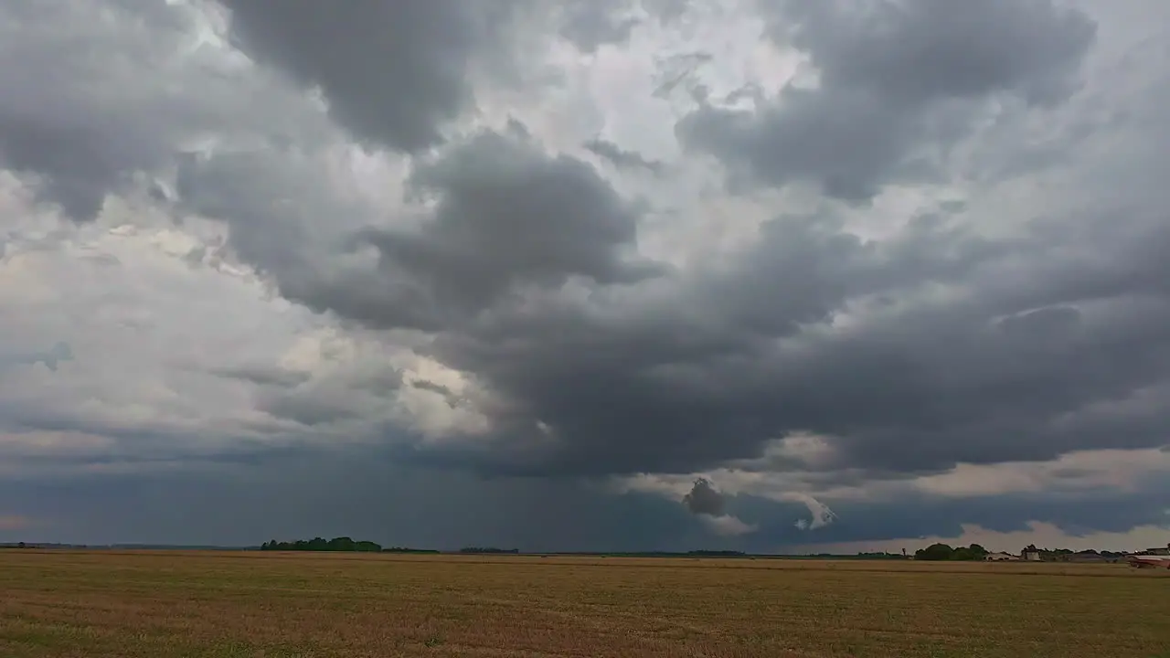 Dark rotating clouds announce a tornado above the fields where a harvester is driving away