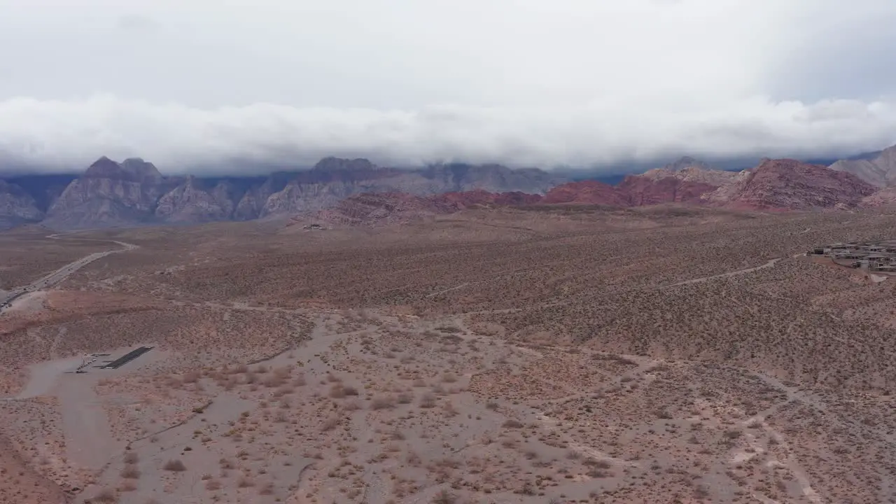 Wide descending aerial shot of Red Rock Canyon with thick clouds over the mountains in Las Vegas Nevada