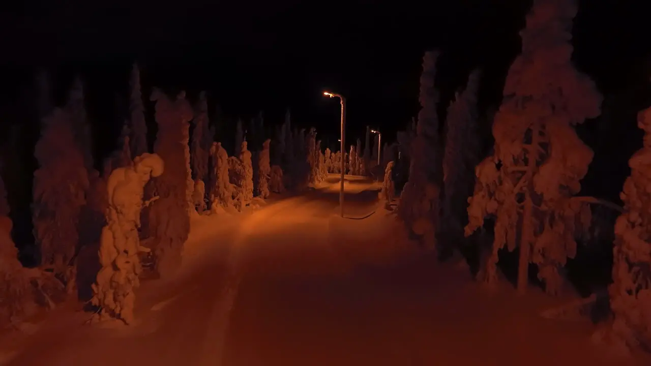 Aerial view rising over a night lit road in middle of snow covered trees of Lapland