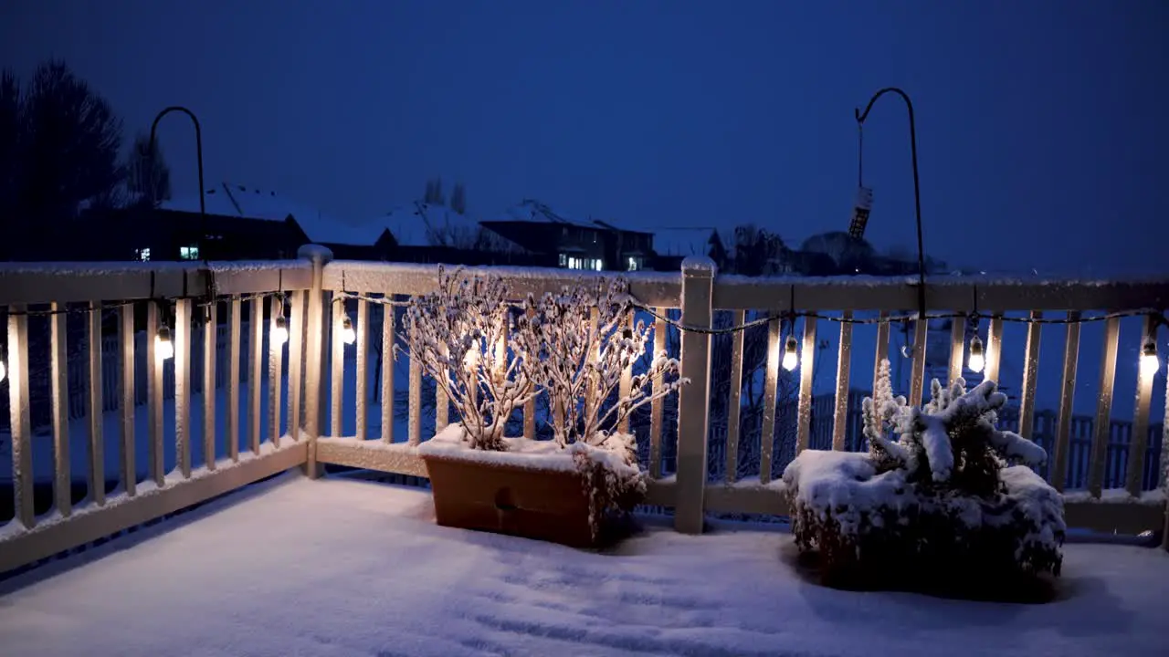 Cold winter snowy night as seen from an urban backyard deck with the porch lights on static wide angle view