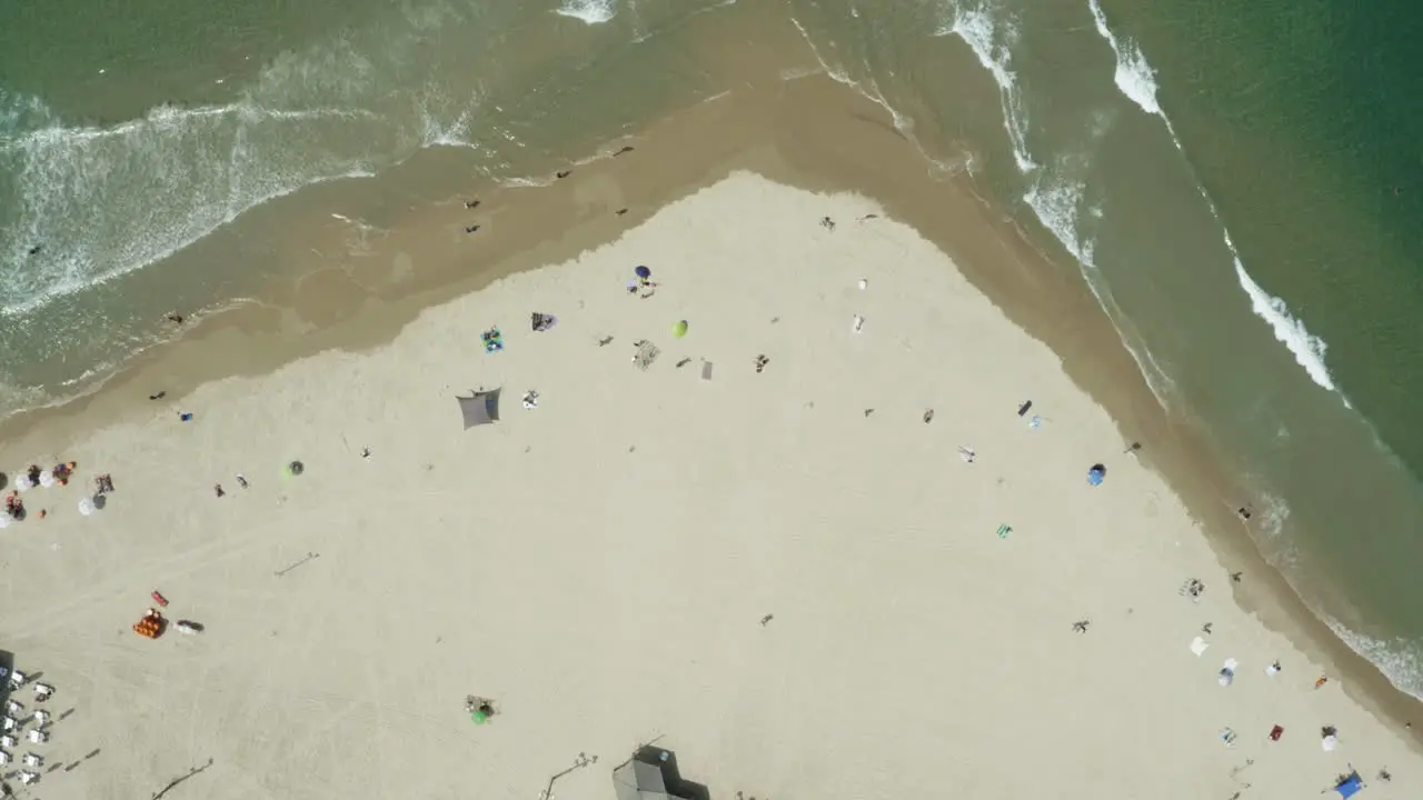 Aerial vertical top down view of calm ocean waves hitting the beach occupied with tourists enjoying the sunny weather at Tel Aviv beach