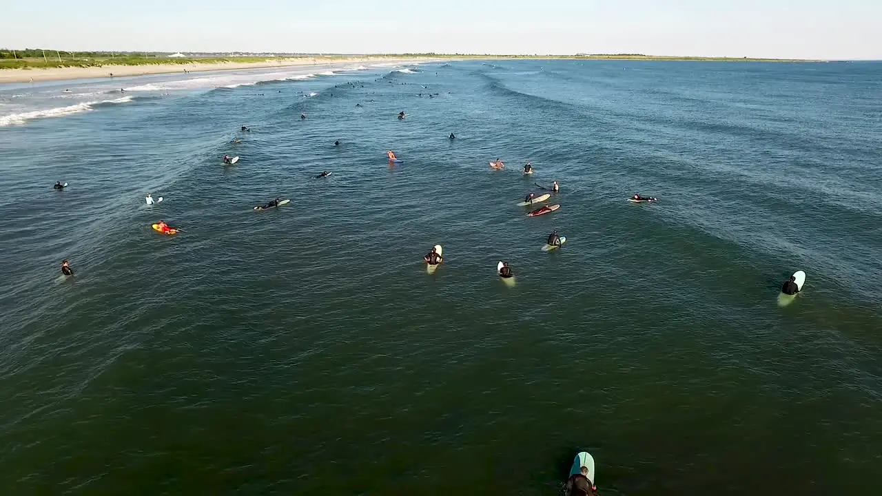 Aerial footage of many surfers riding the waves along the coast of Rhode Island