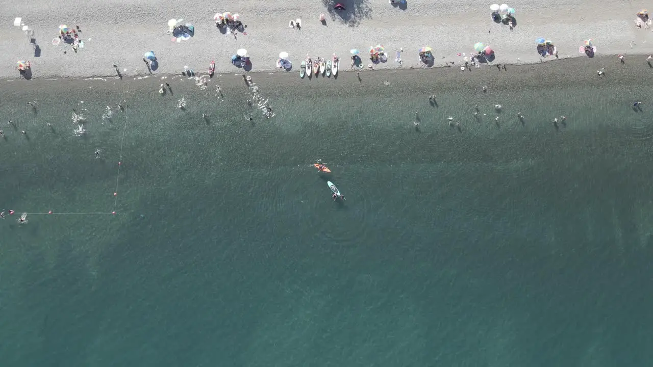 Aerial circling shot of people bathing in the Ranco lake in Chile while there are people practicing paddleboarding