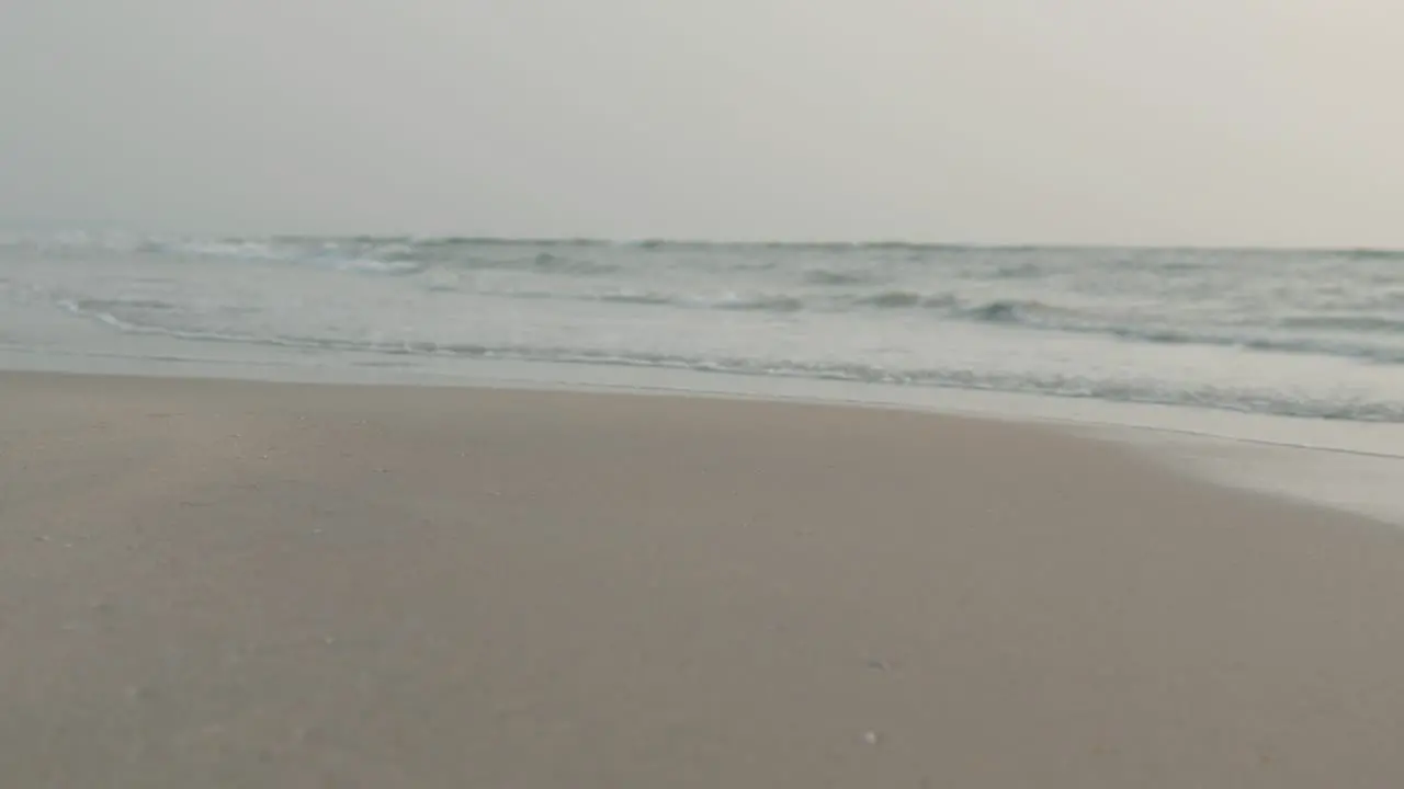 Close view of sandy beach with gentle waves at dusk hint of orange sky on horizon calm atmosphere