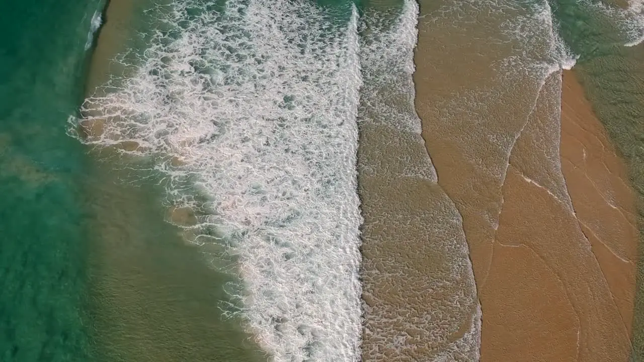 Aerial view of waves breaking over a shallow sand bar close to a popular beach