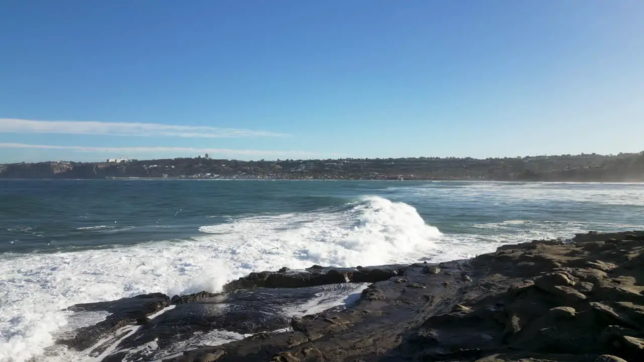 4K slow motion footage of large ocean waves crashing on cliffs at high tide in La Jolla Cove in San Diego California as pelican and white birds flys by