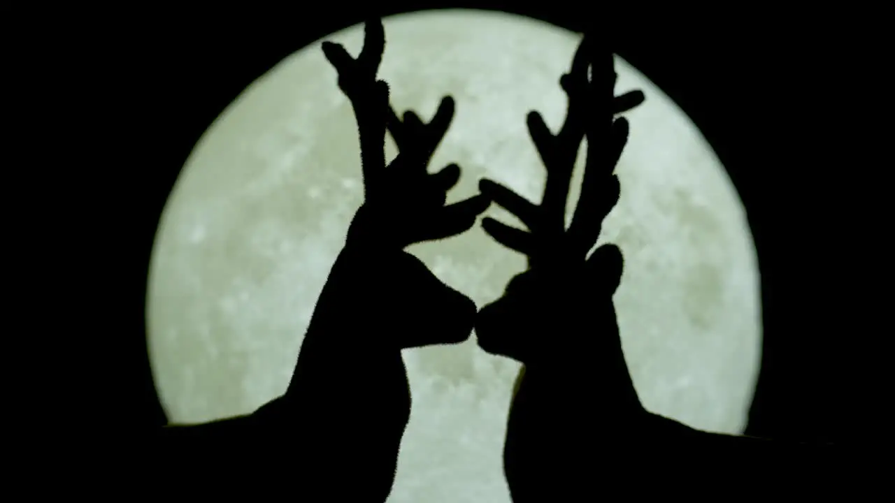 Silhouetted miniature reindeer couple kissing against white moonlight backdrop