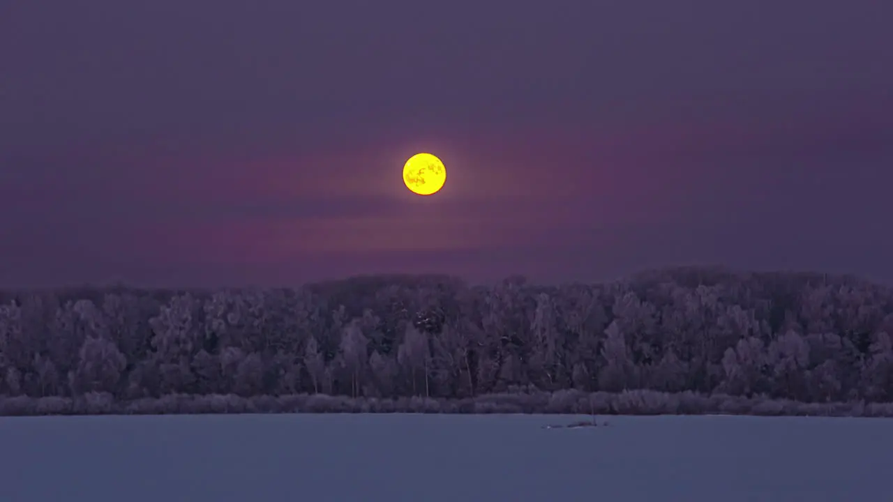 Full moon rising above the winter forest landscape and into the misty clouds nighttime time lapse