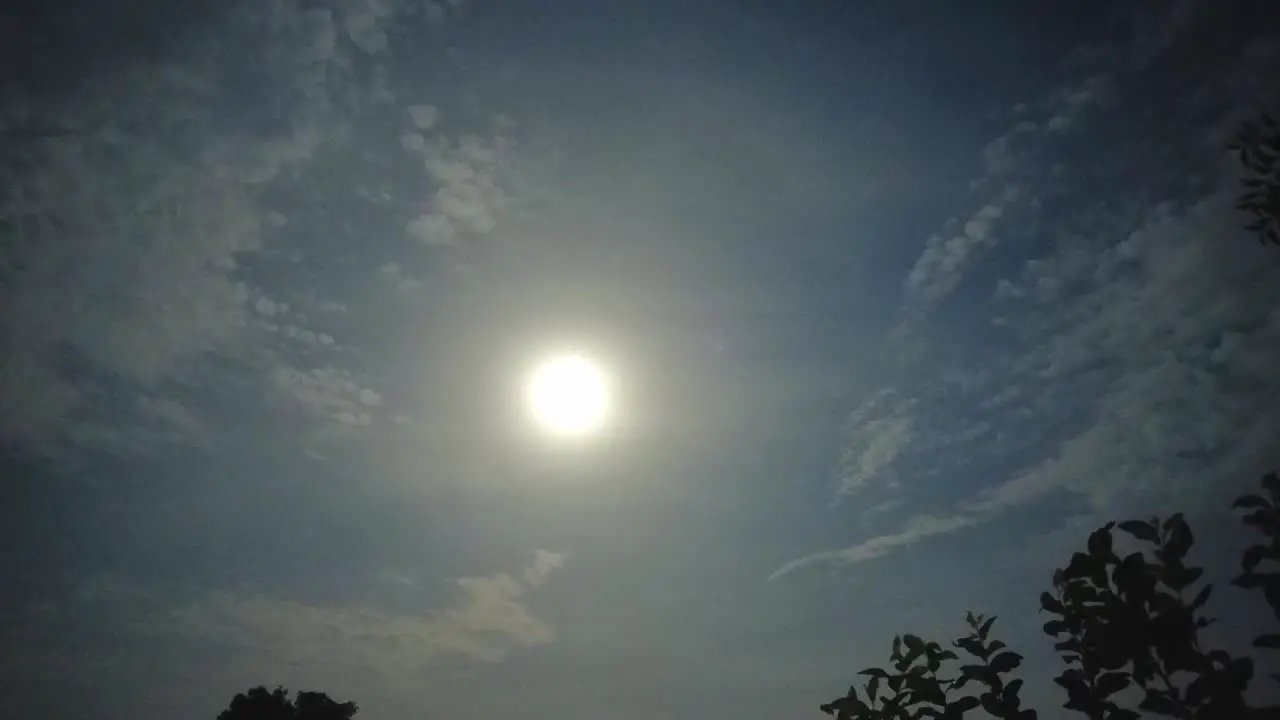 Full moon time lapse with light clouds and visible leaves on the edges