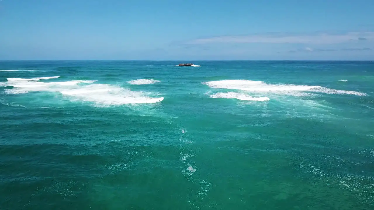 Drone shot flying over a crystal clear blue ocean towards a small isolated rocky island off in the distance