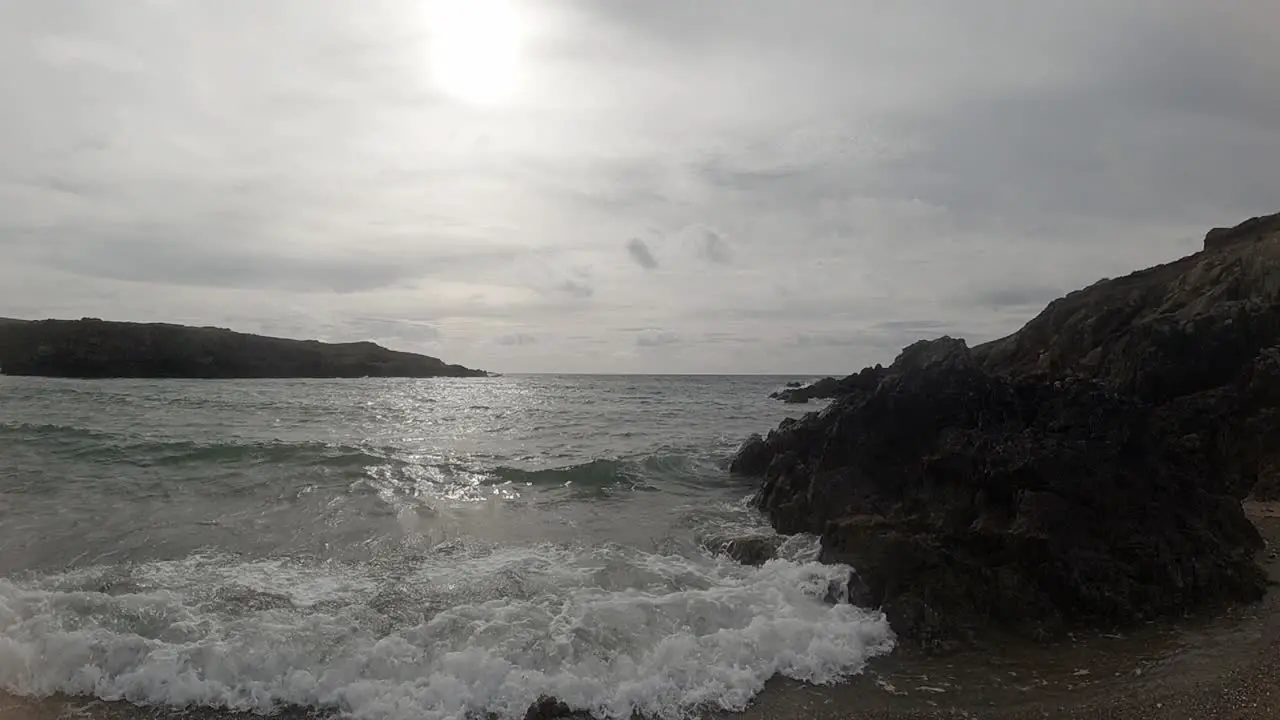 Slow motion foaming ocean tide crashing against rugged Welsh coastline at sunrise