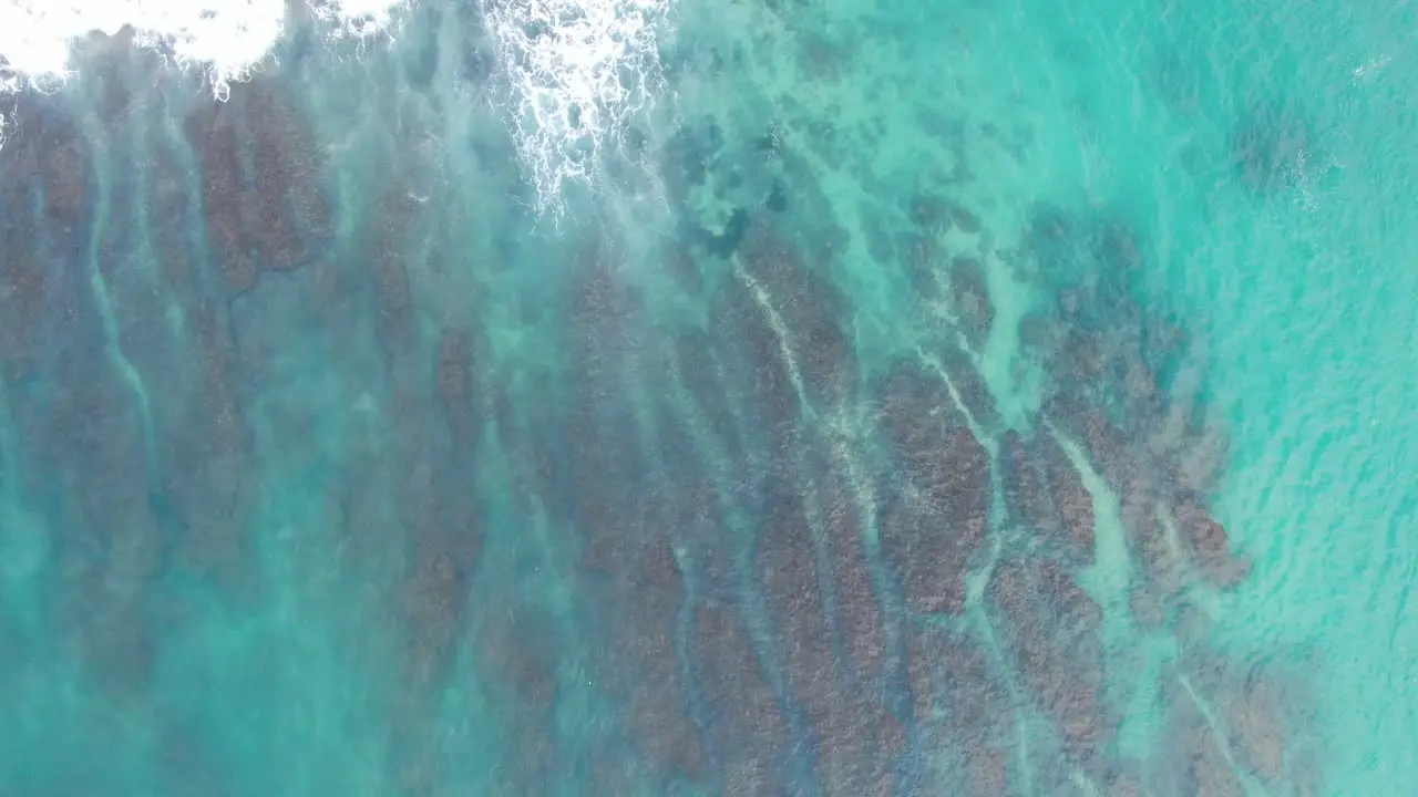 Waves crashing near tropical island aerial top down