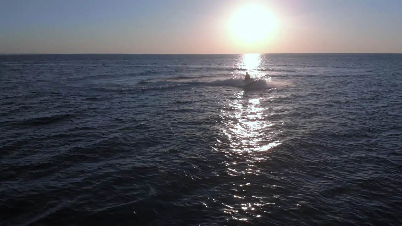 A Woman on a Jet Ski Performs a Tight Turn on an Empty Ocean During Sunset Static Drone View