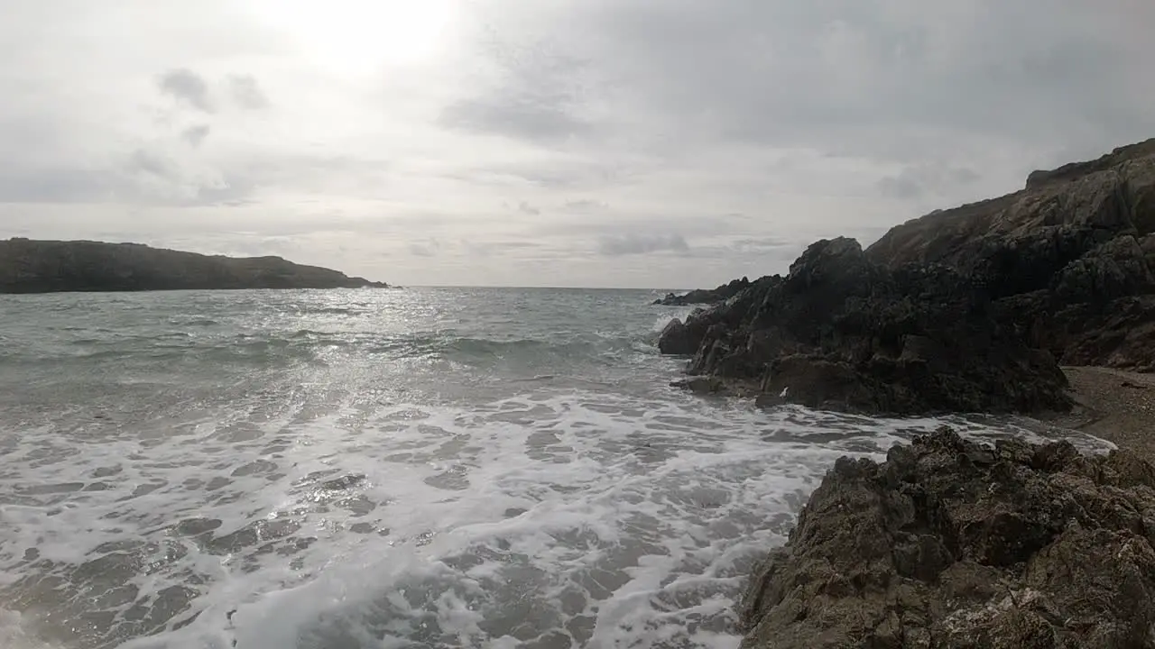 Slow motion foaming ocean tide crashing against rugged Welsh waterfront at sunrise