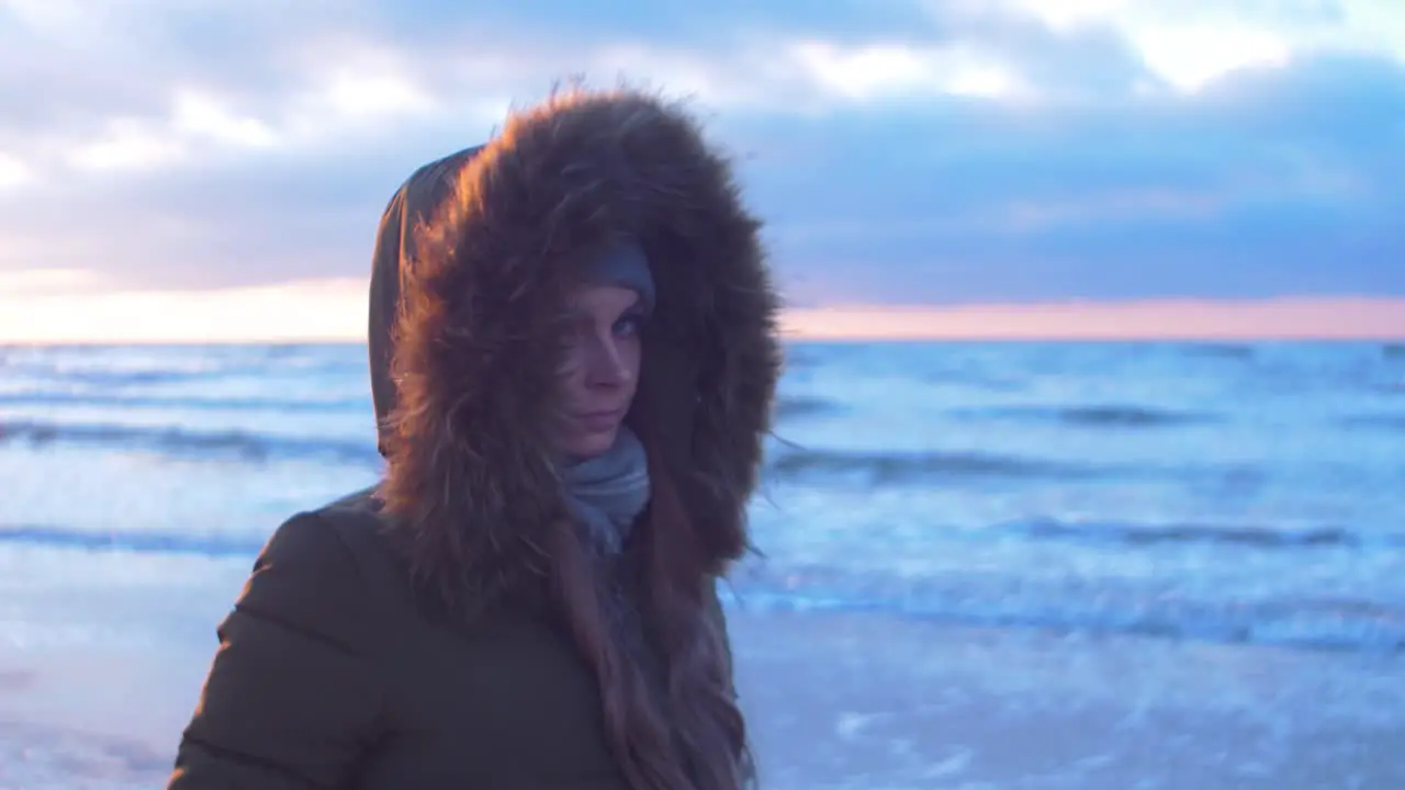 Young woman in winter clothes walks along the sandy shore of the Baltic sea beach at romantic sunset medium jib shot up