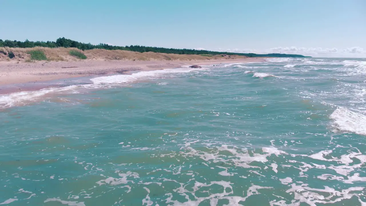 Aerial flying over waves crashing onto a pink tropical beach with no people