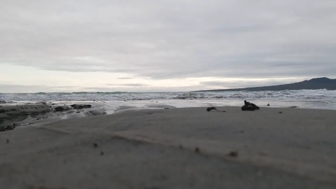 Ground level view of small waves approaching a beach with dark sand on New Zealand's north island