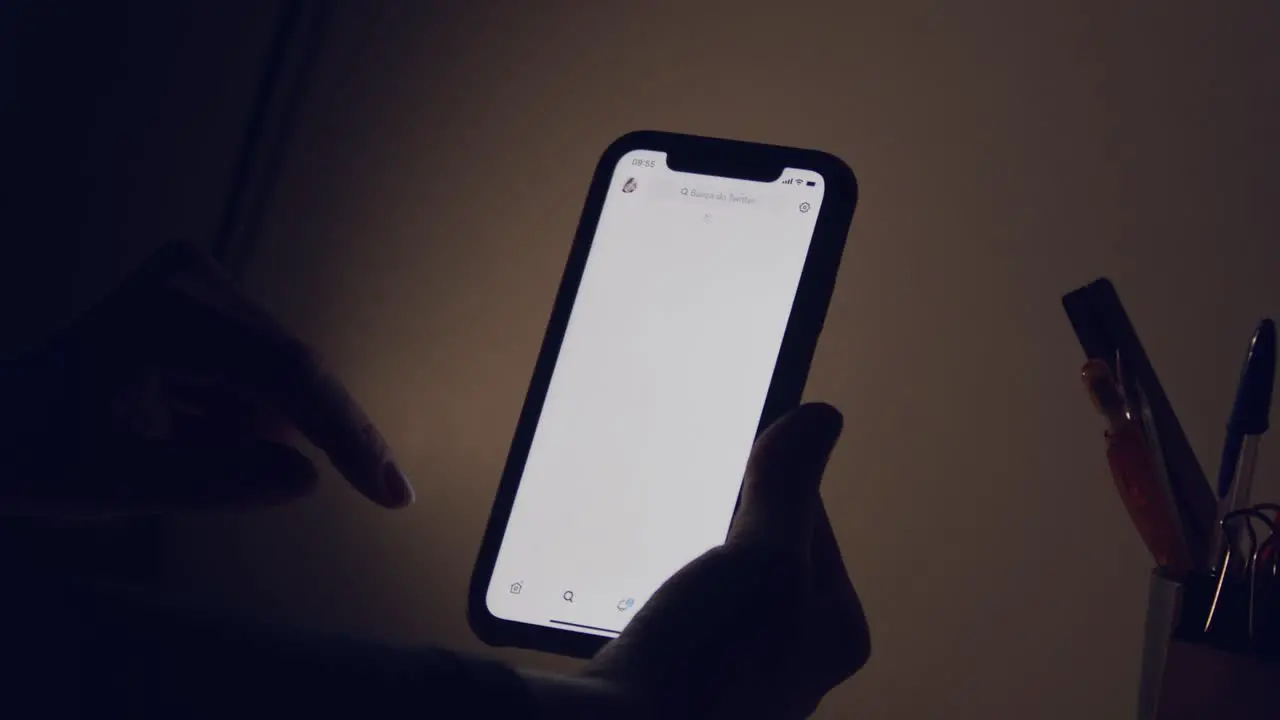 The glowing screen of a smartphone as a woman's hand scrolls through Twitter