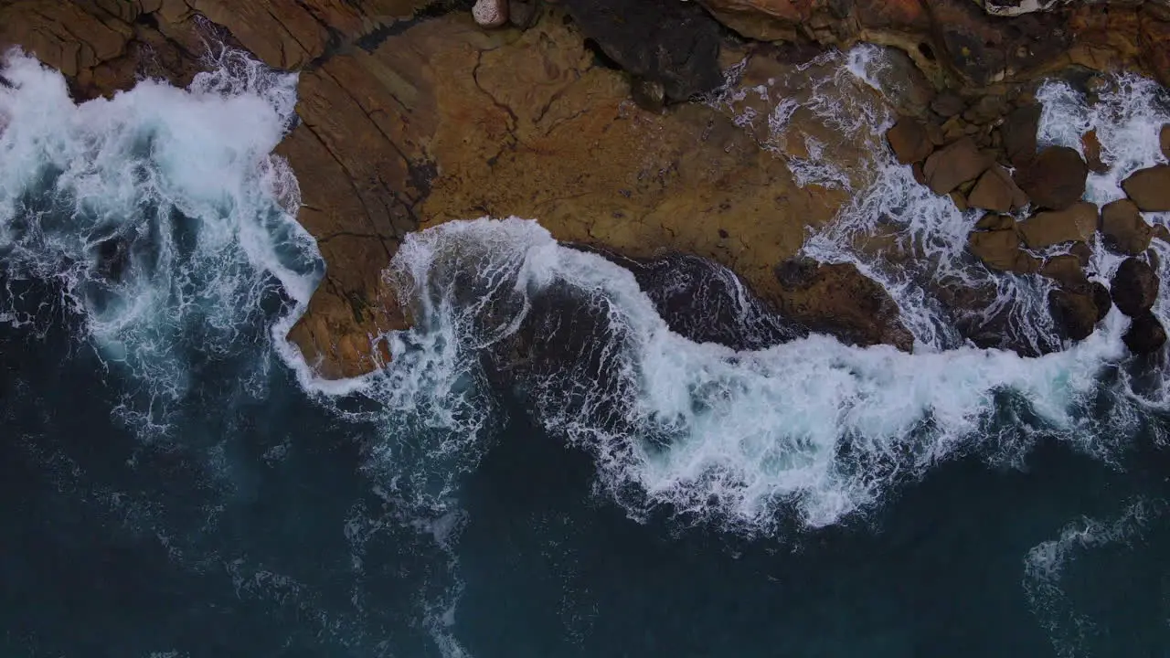 Above drone shot of rocks being lapped with waves