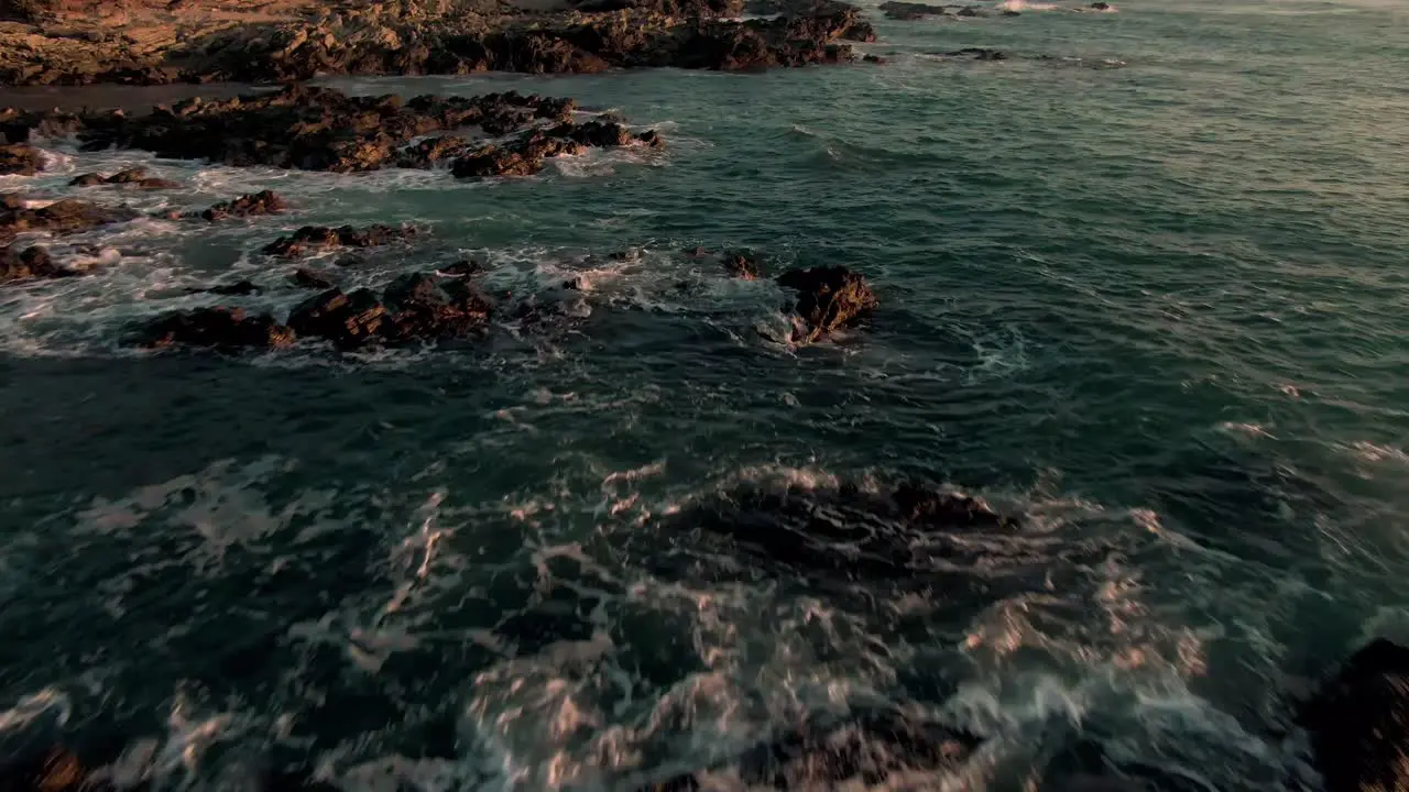 Drone parallax flight above breaking swell on rocky Costa Rica beach in sunset