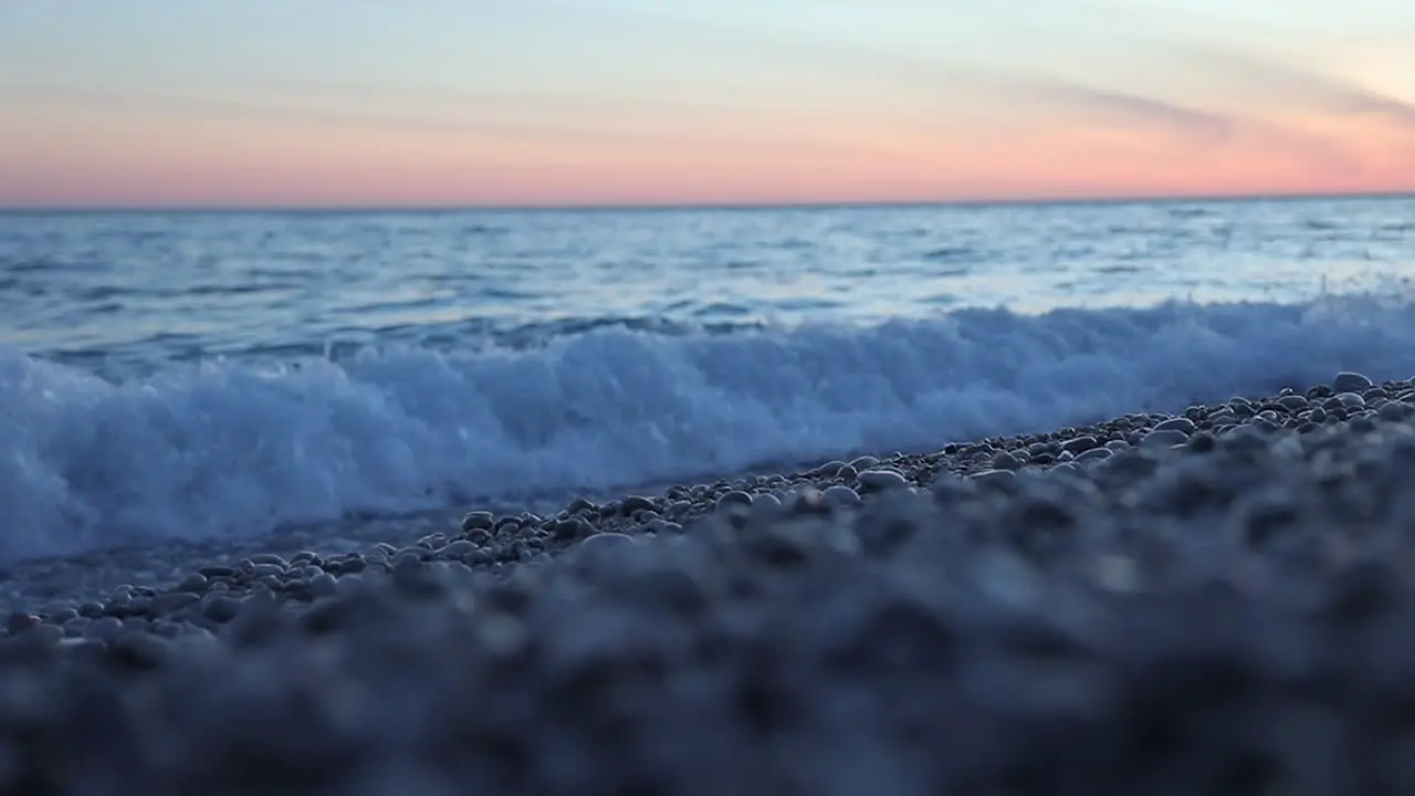 Sea wave washing pebbles beach in slow motion during colorful sunset