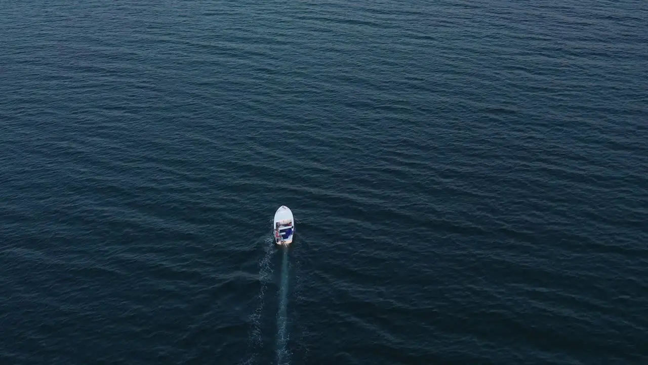 Aerial drone follows small white boat across expanse of open water