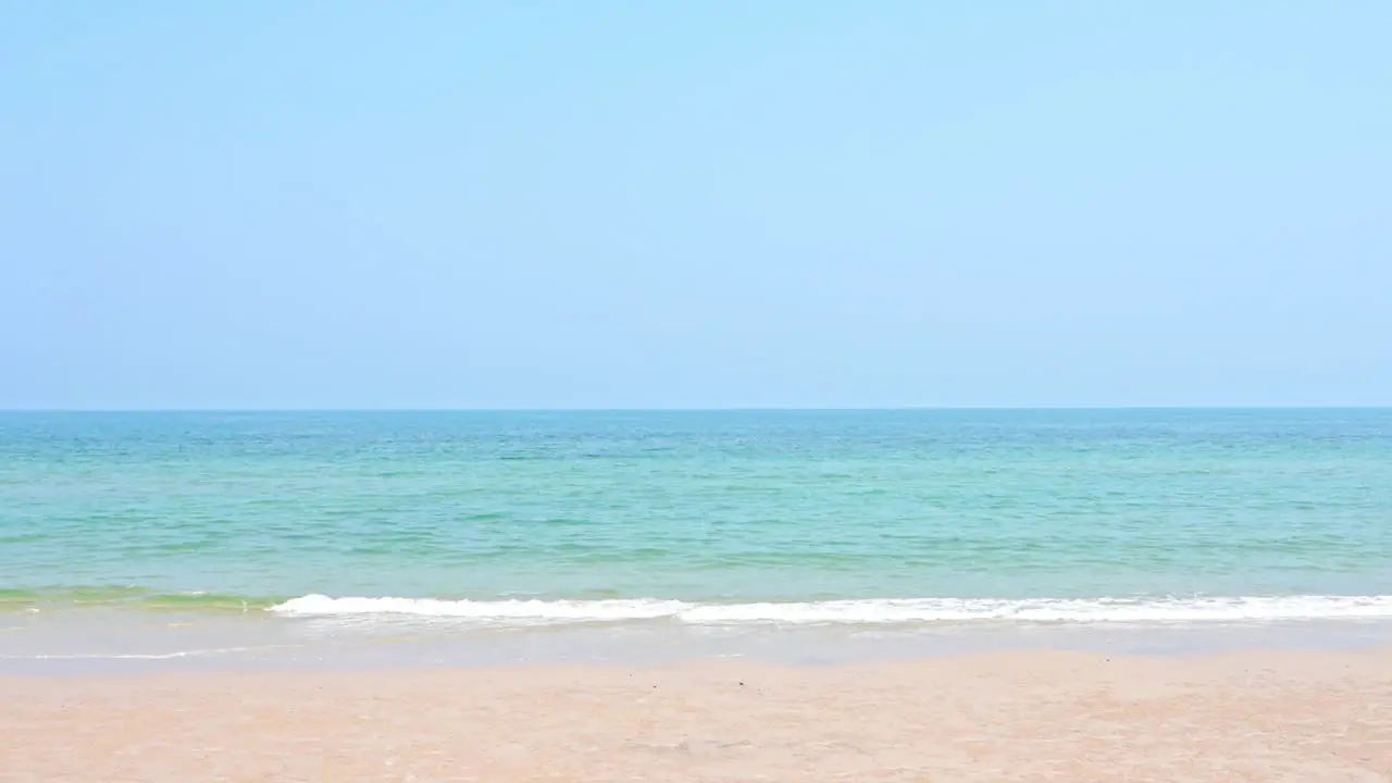 Empty Sandy Beach and Emerald Tranquil Sea Foamy Tides Rolling on Sand on Uninhabited Island In Thailand Cloudless Sky Vacation Template copy space Minimalistic no people