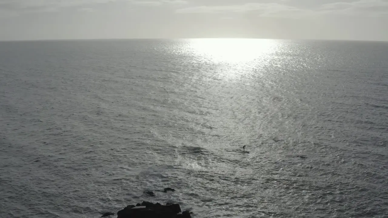 Grey ocean aerial ascends retreats from SUP paddleboarder near rocks