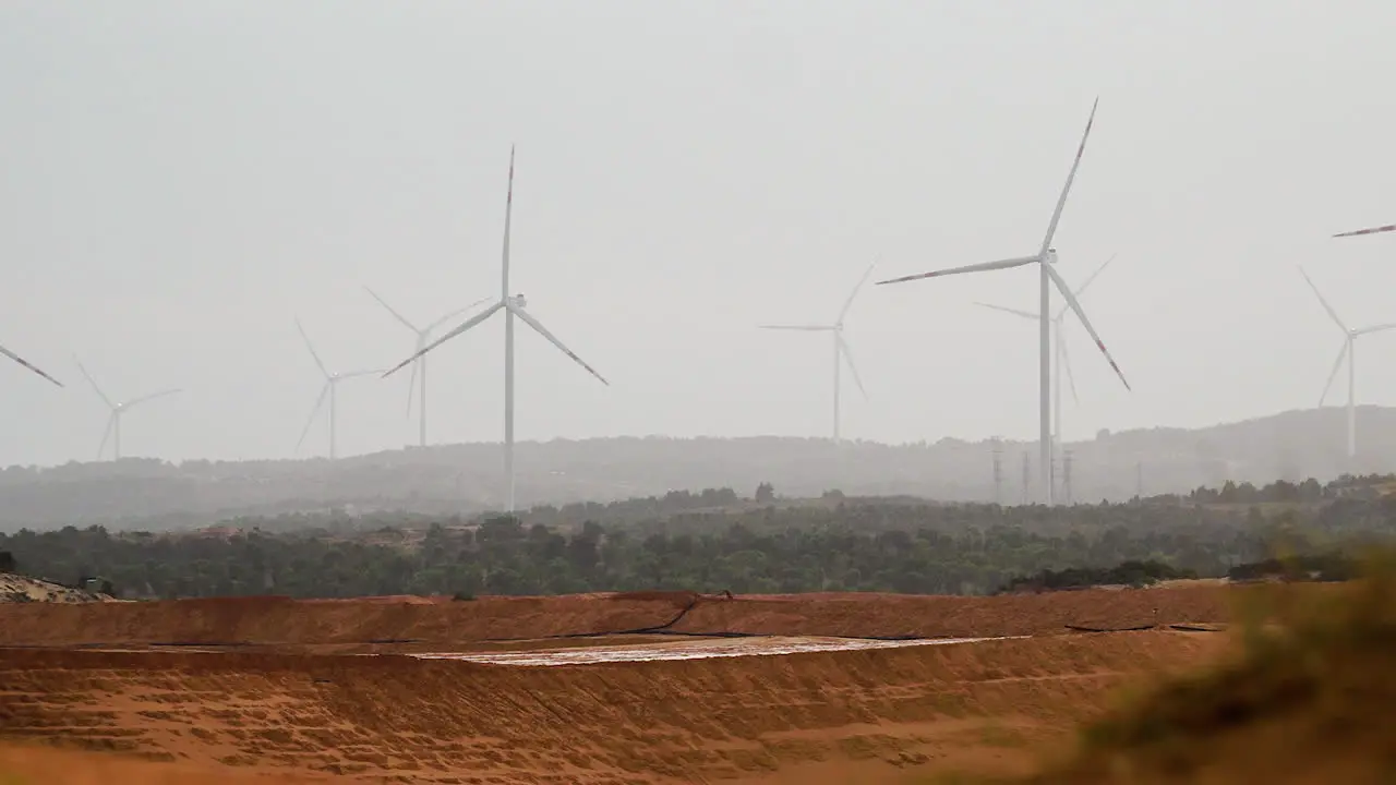 Slow zoom out wind turbine propellers spinning in hot hazy field generating renewable sustainable energy