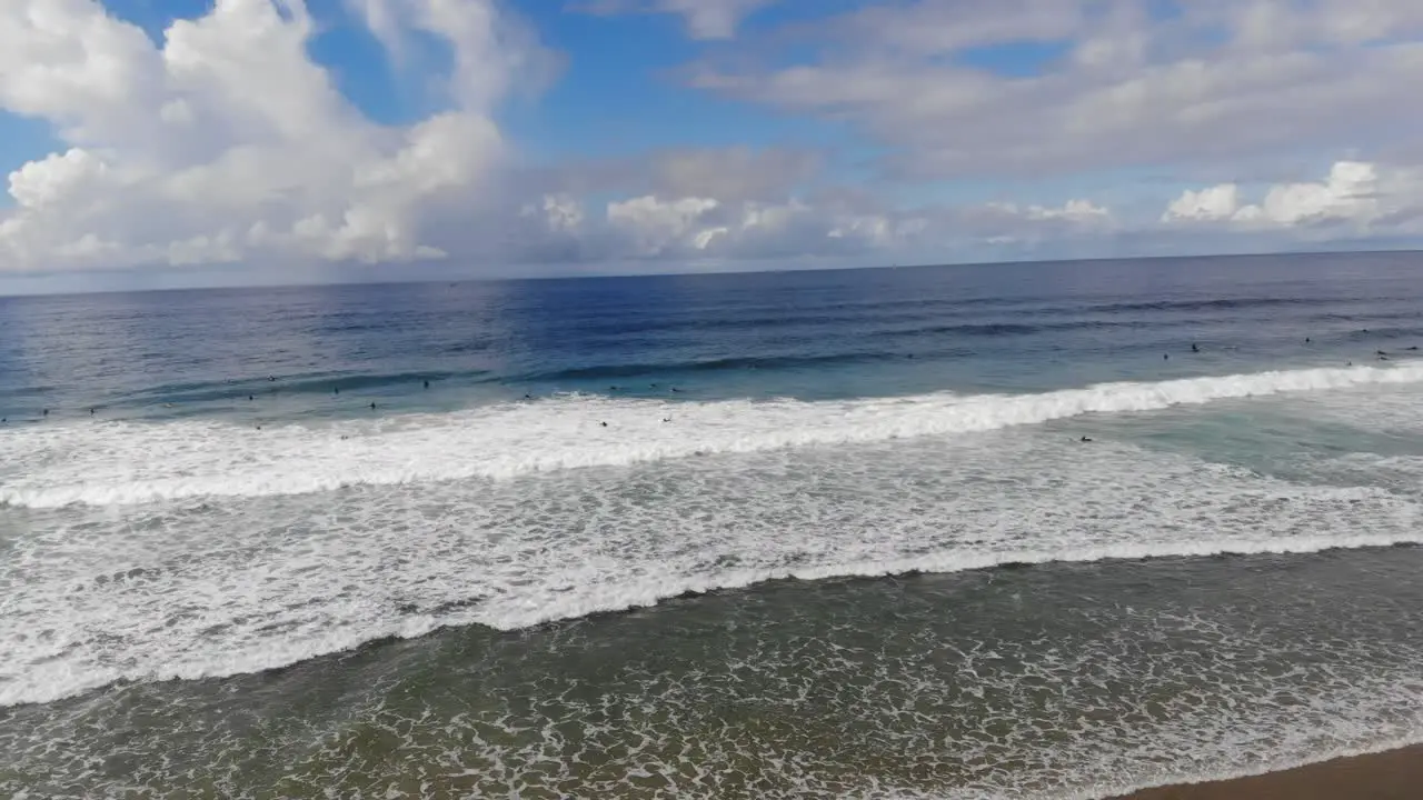 A drone rotates and twists over crashing waves revealing surfers surfing at the beach